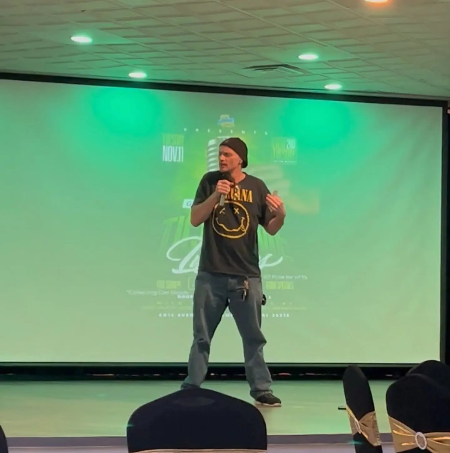 A comedian on the stage in front of the screen at The Heights