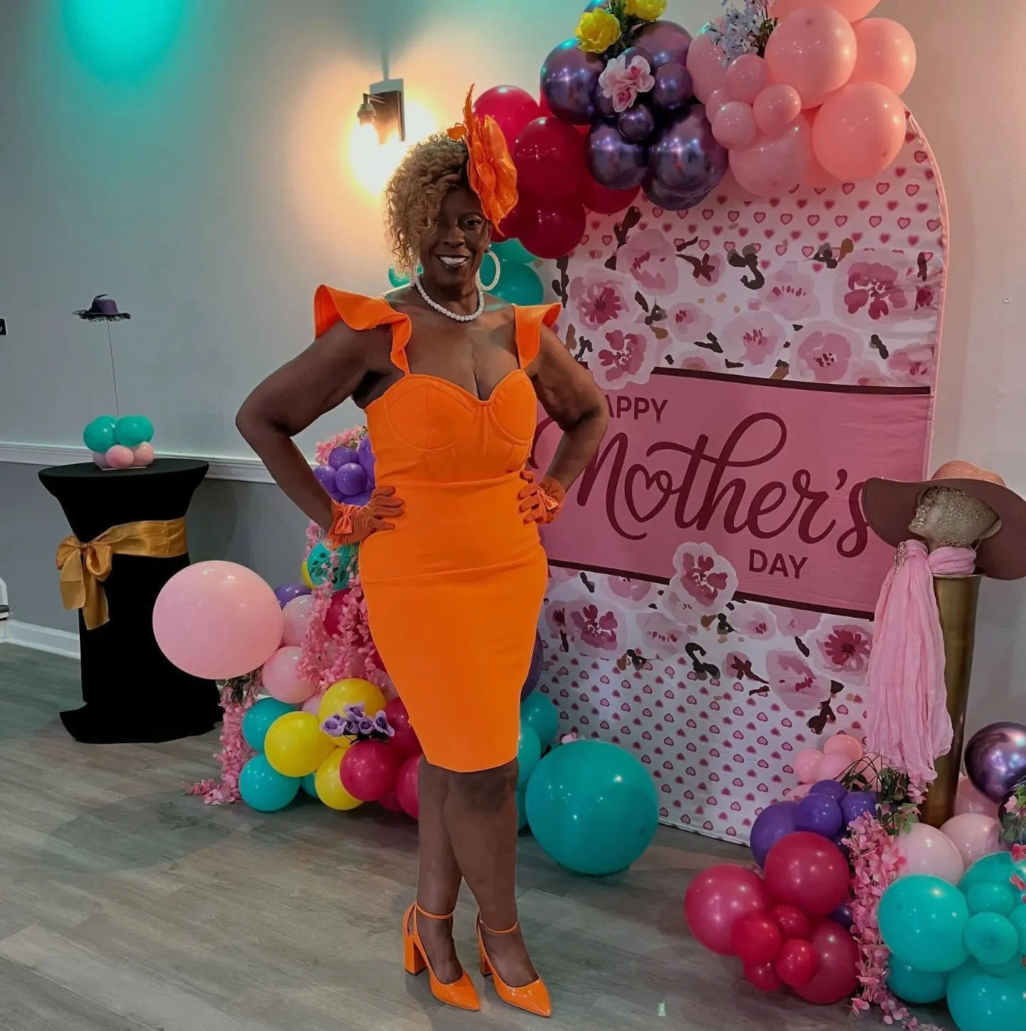 Host in an orange dress by the Mother’s Day balloon backdrop at The Heights