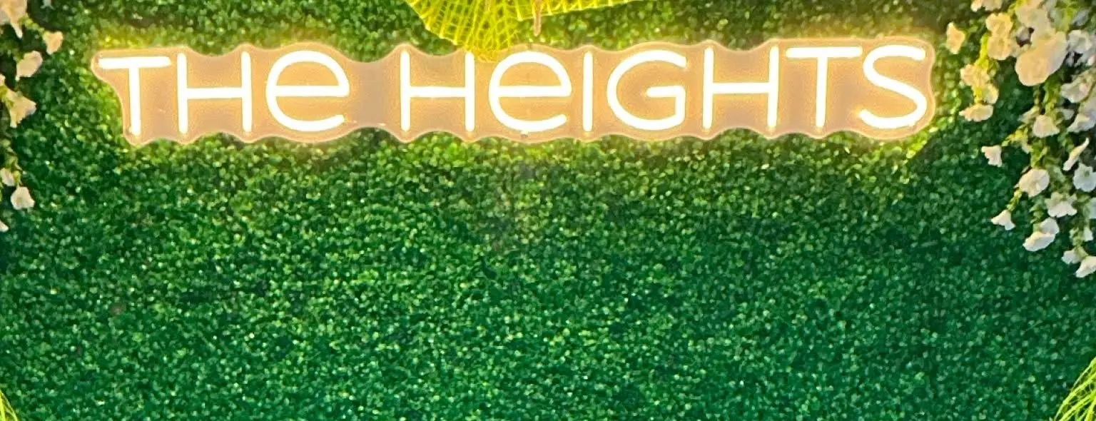 The neon The Heights sign over the greenery wall